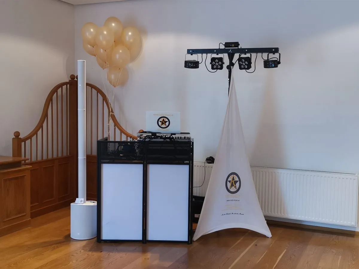Weiße Säulen-PA und DJ-Tisch mit Logo-Laptop, daneben Ballons und eine Lichtanlage auf Stativ