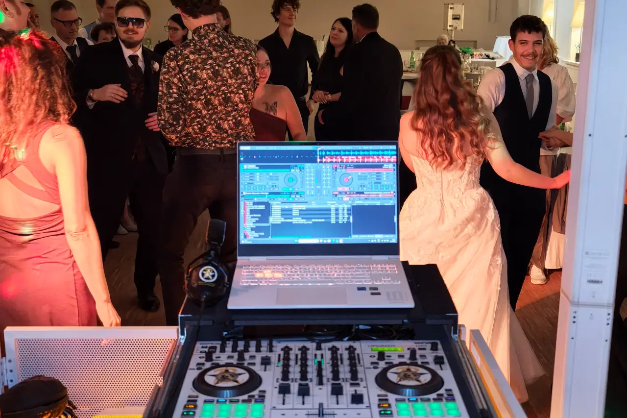 Weißer DJ-Controller mit Laptop am DJ-Pult, dahinter tanzen die Braut und die Gäste bei einer Hochzeit im Restaurant Henrici